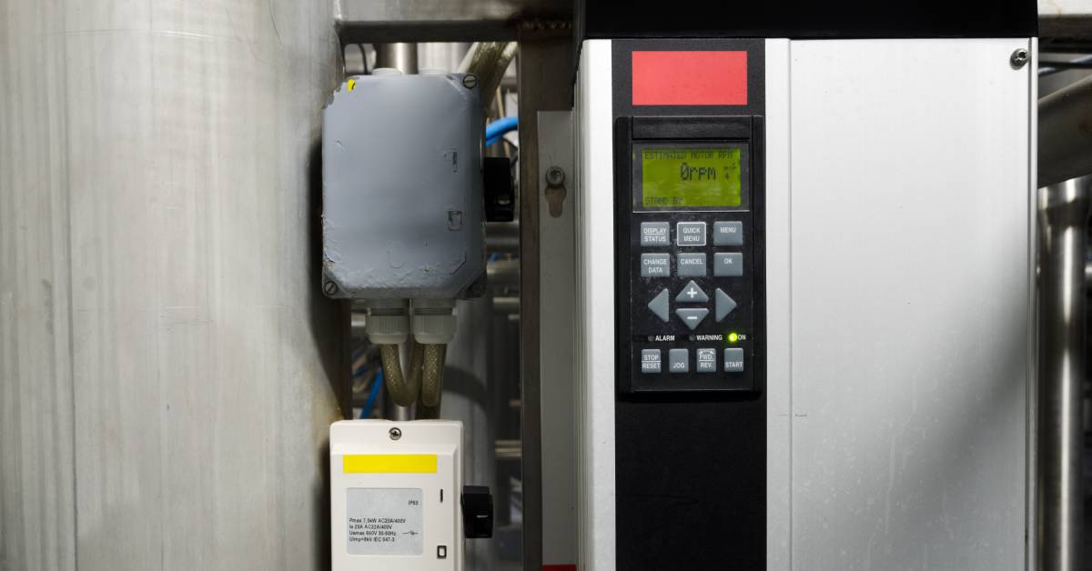 A lit display with a button control pad on a frequency converter in an industrial setting. The screen reads "0 rpm".